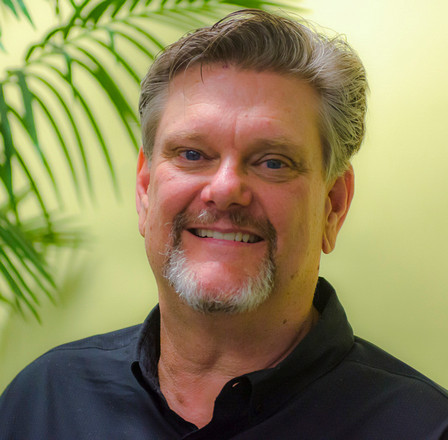 Portrait of David Benson, smiling, in front of palm fronds